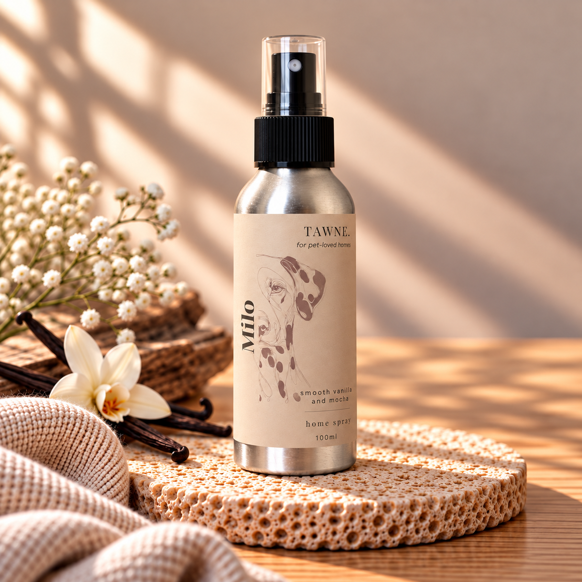 A 100ml home spray bottle by Tawne  labeled 'Milo', set on a woven tray with a beige linen cloth and dried flowers in a warm, sunlit setting.