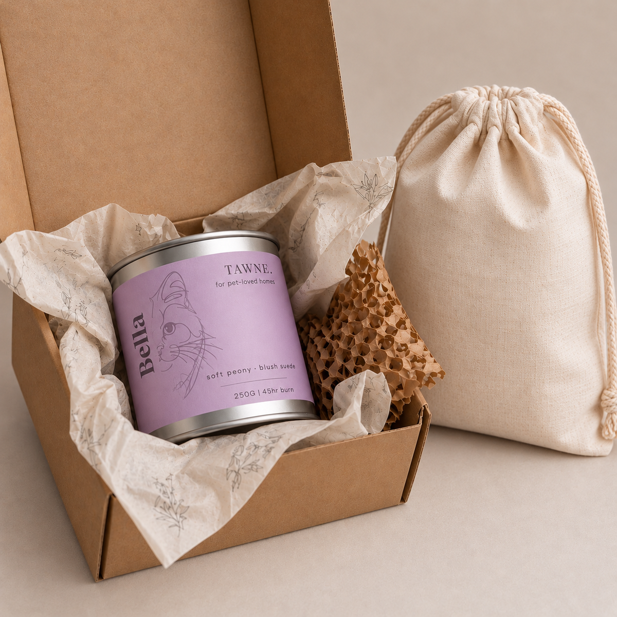 A packaged order containing a candle tin labeled 'Tawne', nestled in tissue paper inside a brown kraft box, next to a beige drawstring pouch.